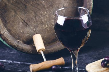 Bardak ve şarap, ahşap fıçının yanında. Yanmış, siyah ahşap arka plan. Eski model. Bir metin için kopyalanmış boşluk. Üzüm ve yeşil üzüm. 