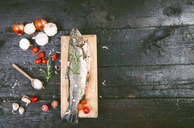 Siyah, yanmış bir masada taze balık. Tahta masa. Sebzeli balık, tuz, yağ, otlar. Yemek pişirme kavramı. Sağlıklı ve diyet yapan yiyecekler. Ayrıntı