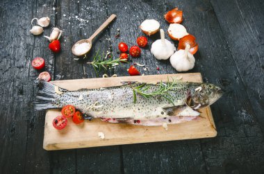 Siyah, yanmış bir masada taze balık. Tahta masa. Sebzeli balık, tuz, yağ, otlar. Yemek pişirme kavramı. Sağlıklı ve diyet yapan yiyecekler. Ayrıntı