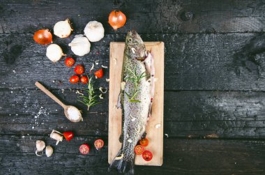 Siyah, yanmış bir masada taze balık. Tahta masa. Sebzeli balık, tuz, yağ, otlar. Yemek pişirme kavramı. Sağlıklı ve diyet yapan yiyecekler. Ayrıntı