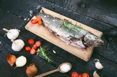 Siyah, yanmış bir masada taze balık. Tahta masa. Sebzeli balık, tuz, yağ, otlar. Yemek pişirme kavramı. Sağlıklı ve diyet yapan yiyecekler. Ayrıntı