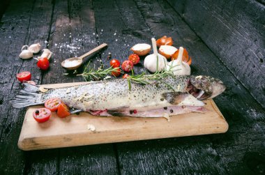Siyah, yanmış bir masada taze balık. Tahta masa. Sebzeli balık, tuz, yağ, otlar. Yemek pişirme kavramı. Sağlıklı ve diyet yapan yiyecekler. Ayrıntı