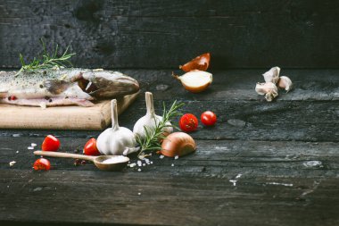 Siyah, yanmış bir masada taze balık. Tahta masa. Sebzeli balık, tuz, yağ, otlar. Yemek pişirme kavramı. Sağlıklı ve diyet yapan yiyecekler. Ayrıntı
