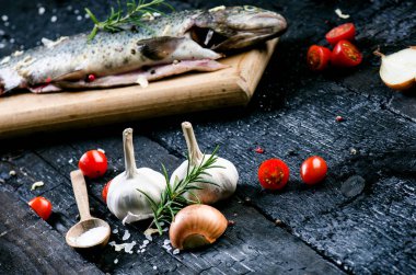 Siyah, yanmış bir masada taze balık. Tahta masa. Sebzeli balık, tuz, yağ, otlar. Yemek pişirme kavramı. Sağlıklı ve diyet yapan yiyecekler. Ayrıntı