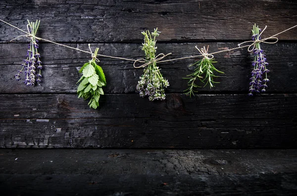 Lavanta çiçekleri, biberiye, nane, kekik, Melissa ve siyah tahta bir masanın üzerinde eski bir makas. Yanmış odun. Spa ve kozmetik veya aşçılık arka planı.