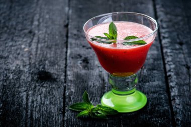 Tahta yanmış bir masada buz küpleriyle taze kavun dilimleri ile su karpuzu kokteyli. Siyah doğal arka plan. Sağlıklı bir içki. Yaz kokteyli