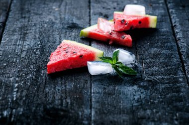 Tahta yanmış bir masada buz küpleriyle taze kavun dilimleri ile su karpuzu kokteyli. Siyah doğal arka plan. Sağlıklı bir içki. Yaz kokteyli