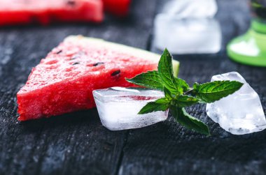 Tahta yanmış bir masada buz küpleriyle taze kavun dilimleri ile su karpuzu kokteyli. Siyah doğal arka plan. Sağlıklı bir içki. Yaz kokteyli