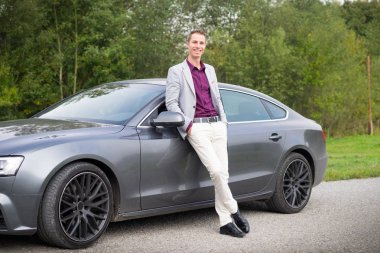 Genç, mutlu, arabadaki iş adamı. Takım elbiseli bir adam pahalı spor arabanın yanında duruyor. Başarılı genç adam..