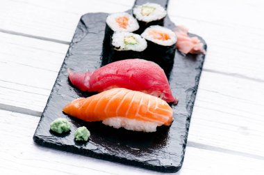 Suşi seti siyah bir levhada servis edilir. Suşi ruloları ve saşimi ahşap beyaz bir masada. Deniz ürünleri. Çiğ balık. Beyaz arka plan. Wasabi.. 