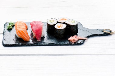 Suşi seti siyah bir levhada servis edilir. Suşi ruloları ve saşimi ahşap beyaz bir masada. Deniz ürünleri. Çiğ balık. Beyaz arka plan. Wasabi.. 
