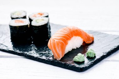 Suşi seti siyah bir levhada servis edilir. Suşi ruloları ve saşimi ahşap beyaz bir masada. Deniz ürünleri. Çiğ balık. Beyaz arka plan. Wasabi.. 