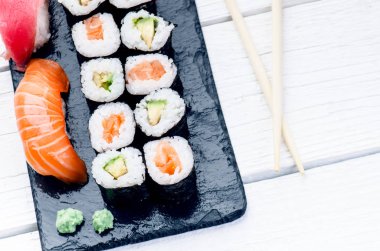 Suşi seti siyah bir levhada servis edilir. Suşi ruloları ve saşimi ahşap beyaz bir masada. Deniz ürünleri. Çiğ balık. Beyaz arka plan. Wasabi.. 