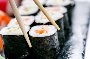 Suşi seti siyah bir levhada servis edilir. Suşi ruloları ve saşimi ahşap beyaz bir masada. Deniz ürünleri. Çiğ balık. Beyaz arka plan. Wasabi.. 