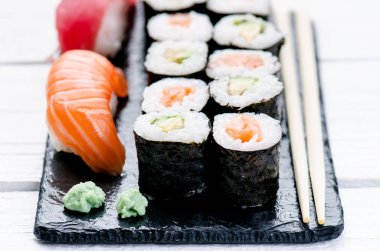 Suşi seti siyah bir levhada servis edilir. Suşi ruloları ve saşimi ahşap beyaz bir masada. Deniz ürünleri. Çiğ balık. Beyaz arka plan. Wasabi.. 