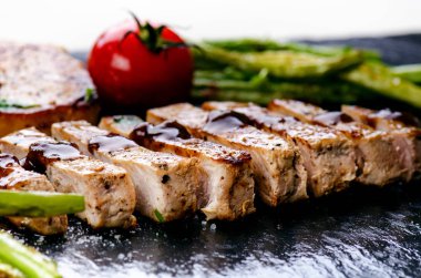 Izgara domuz pirzolası, sebzeli biftek, domates, fasulye ve siyah tahtada sos. Köpüklü taze et. Karanlık arka plan. Izgara ve barbekü konsepti. 