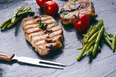 Izgara domuz pirzolası, sebzeli biftek, domates, fasulye ve siyah tahtada sos. Köpüklü taze et. Karanlık arka plan. Izgara ve barbekü konsepti. 