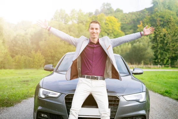 Young, happy, business man in the car. Man in a suits standing by the expensive, sport car. Successful young man.