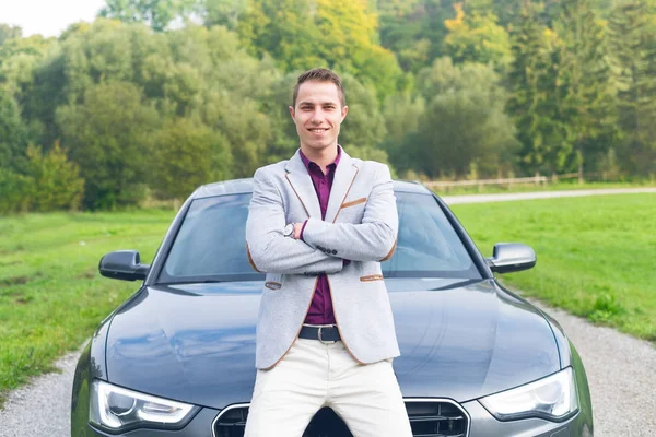 Young, happy, business man in the car. Man in a suits standing by the expensive, sport car. Successful young man.