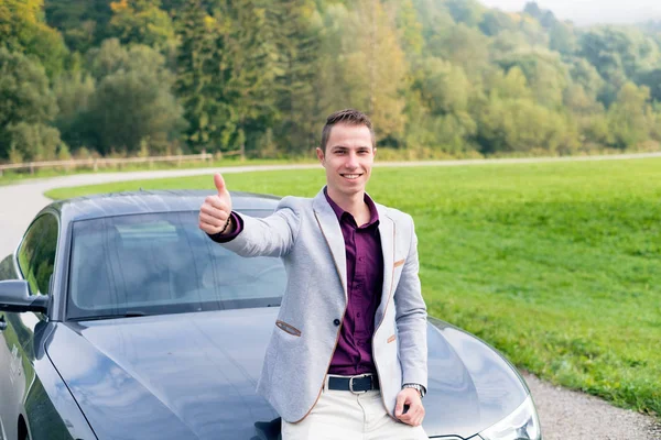 Young, happy, business man in the car. Man in a suits standing by the expensive, sport car. Successful young man.