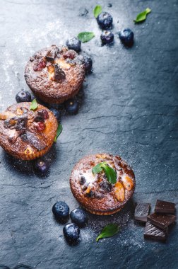 Taze, çilekli yabanmersinli kekler, tahta tahtada çikolata ve şeker ve meyveli taş arka plan. Yemek arkaplanı. Hamur işi kavramı. 