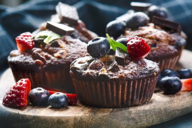 Taze, çilekli yabanmersinli kekler, tahta tahtada çikolata ve şeker ve meyveli taş arka plan. Yemek arkaplanı. Hamur işi kavramı. 