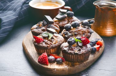 Taze, çilekli yabanmersinli kekler, tahta tahtada çikolata ve şeker ve meyveli taş arka plan. Yemek arkaplanı. Hamur işi kavramı. 