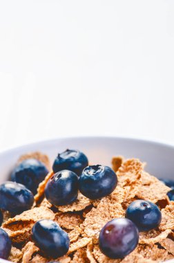 Beyaz bir masada, böğürtlenli ve sütlü müsli kasesi. Sağlıklı kahvaltı gevrekleri. Süt, tohum, meyve. Yulaf gevreği.