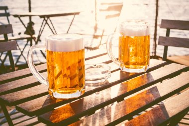 Tahta bir masada köpüklü iki bardak light bira. Teknede. Bahçe partisi. Doğal arka plan. - Alkol. Bira fıçısı. Manzara, altın.