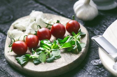 İtalyan yemeği, mutfak. Siyah ahşap bir masada Margherita pizzası. İçinde domates, salata, peynir, mozzarella, fesleğen gibi malzemeler var. Lezzetli ev yemekleri.. 