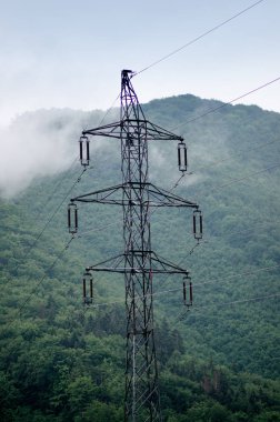 Ormanların ve çayırların ortasındaki yüksek voltaj kuleleri. Karanlık atmosferi olan elektrik direği. Yağmurlu bir gün. Güç aktarım kuleleri.