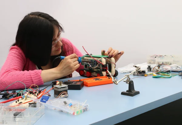 woman with glasses solding a robot