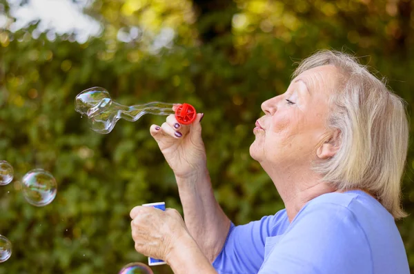 Attractive senior woman blowing soap bubbles — Stock Photo, Image