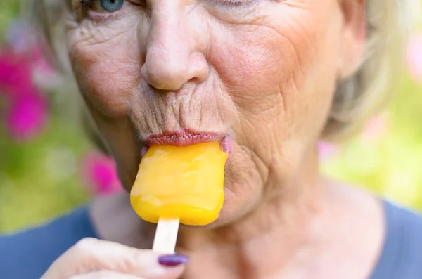 Senior woman sucking on an iced orange lolly — Stock Photo, Image