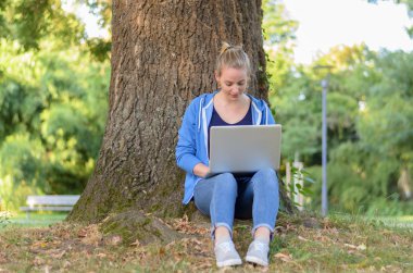 Genç kadın rahatlatıcı bir dizüstü bilgisayar kullanarak bir parkta