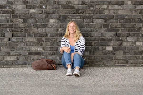 Estudante feminino bonito sentado no chão perto da parede — Fotografia de Stock
