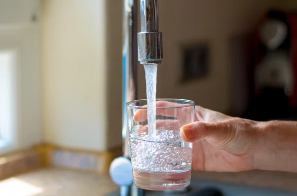 Woman filling a glass of water from a tap — Stockfoto