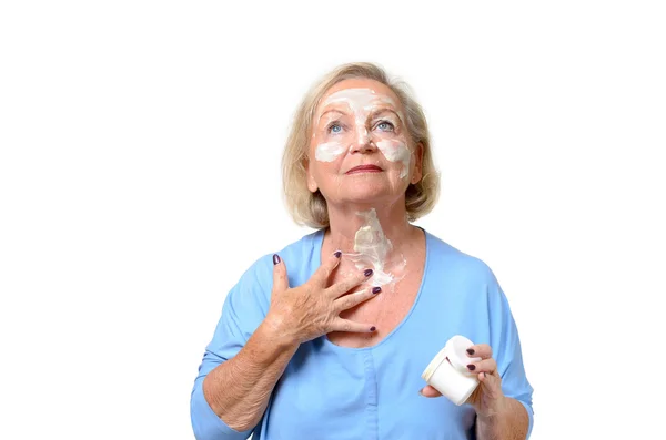 Привлекательная пожилая женщина наносит крем на кожу — стоковое фото