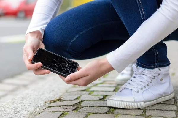 Giovane donna raccogliendo il suo cellulare fracassato — Foto Stock