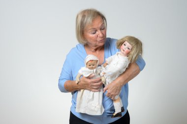 Elderly woman holding two antique dolls clipart