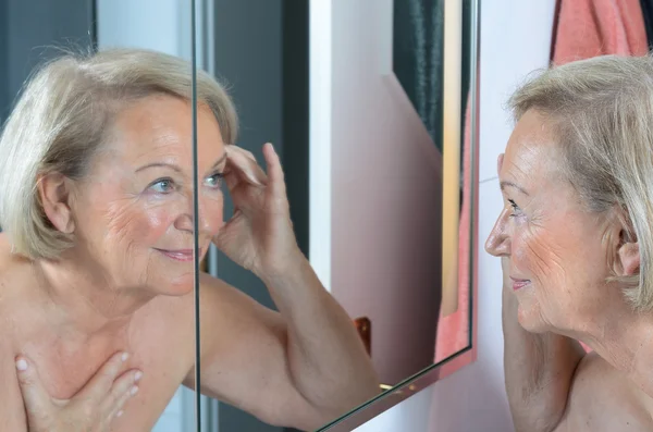 Senior lady checking her skin in the mirror — Stock Photo, Image