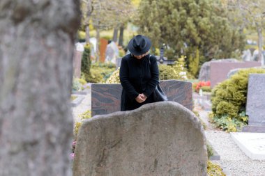 Woman in mourning praying at a graveside clipart
