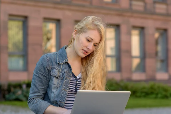 Jovem estudante loira sentado em um banco e trabalhando em seu laptop — Fotografia de Stock