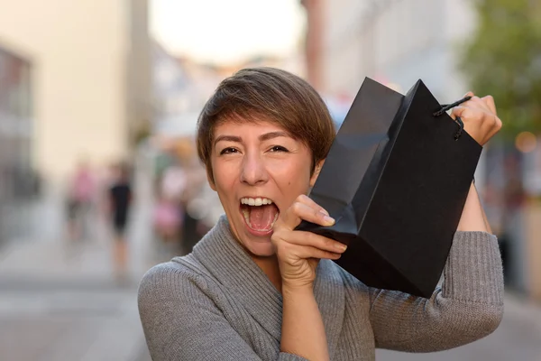 Excited woman holding up a boutique bag — Stock Photo, Image