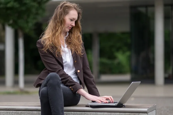 Jovem mulher sentada ao ar livre trabalhando em um laptop — Fotografia de Stock