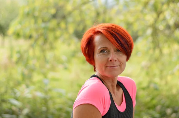 Smiling Adult Woman Against Blurry Green Plants — Stock Photo, Image