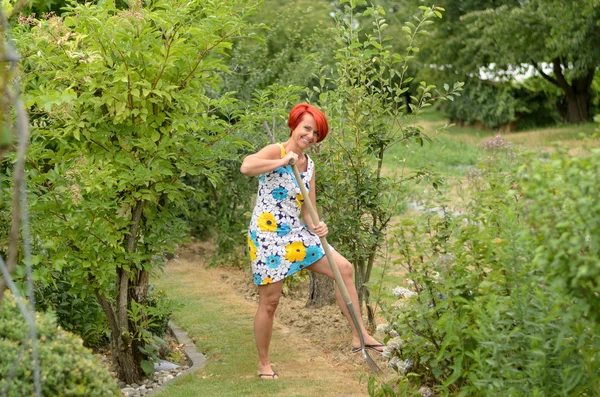 Adulto pelirroja mujer rastrillando el jardín de flores — Foto de Stock