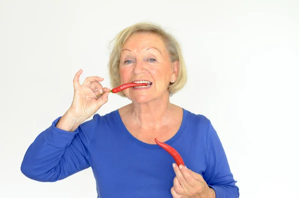 Старшая женщина кусает красный острый перец чили — стоковое фото