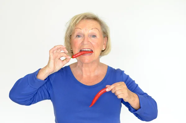 Senior woman biting a red hot chili pepper — Stock Photo, Image