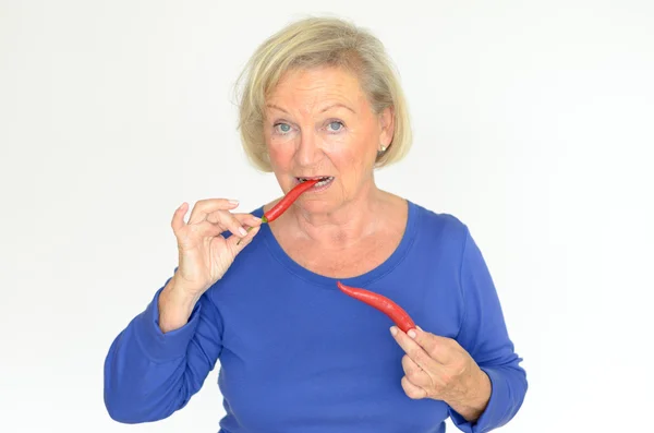 Senior woman biting a red hot chili pepper — Stock Photo, Image